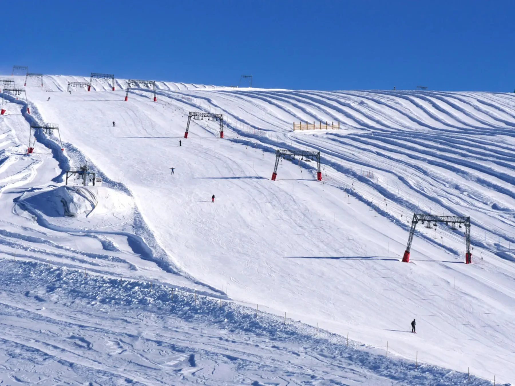 Una pista de esquí nevada con estructuras de remontes y esquiadores bajo un cielo despejado.