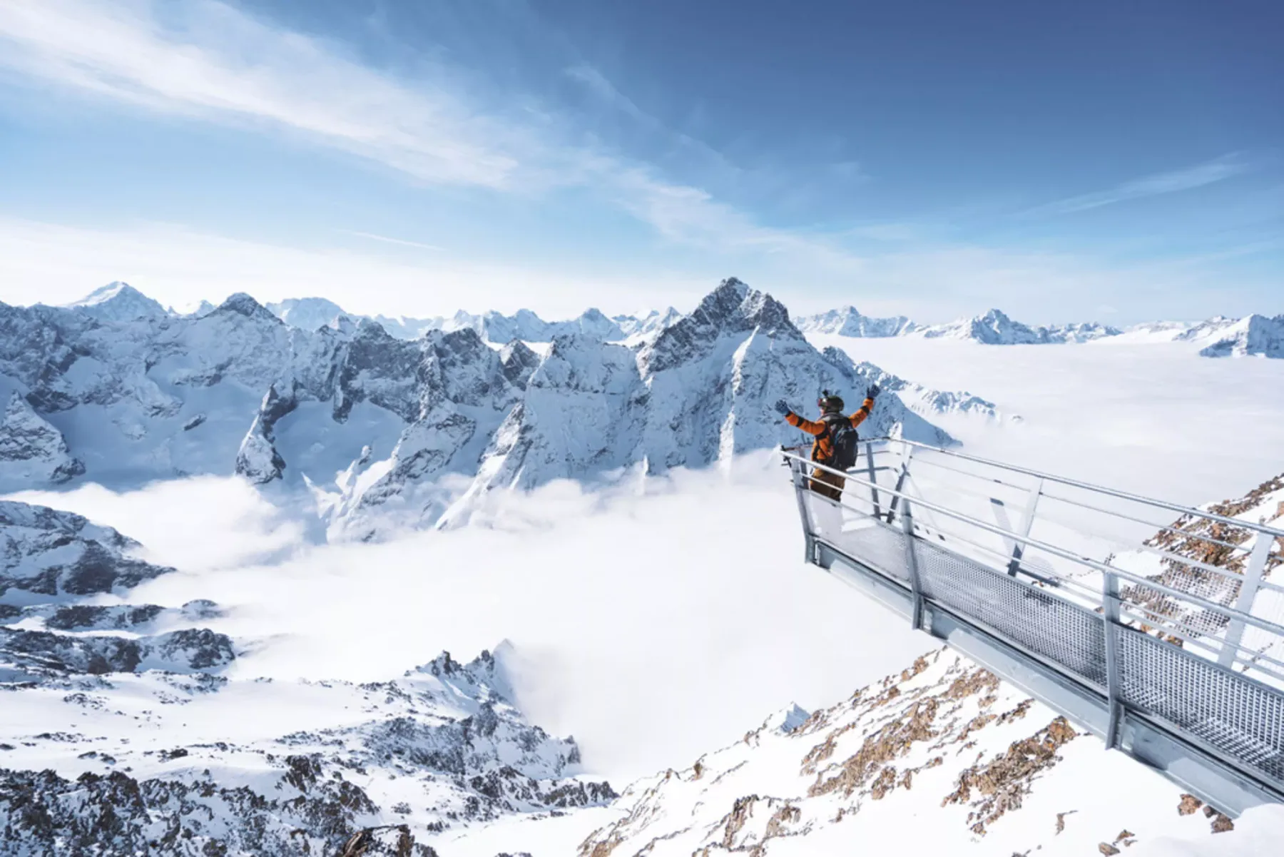 Un mirador de montaña nevado con una persona de pie en una plataforma de observación metálica.