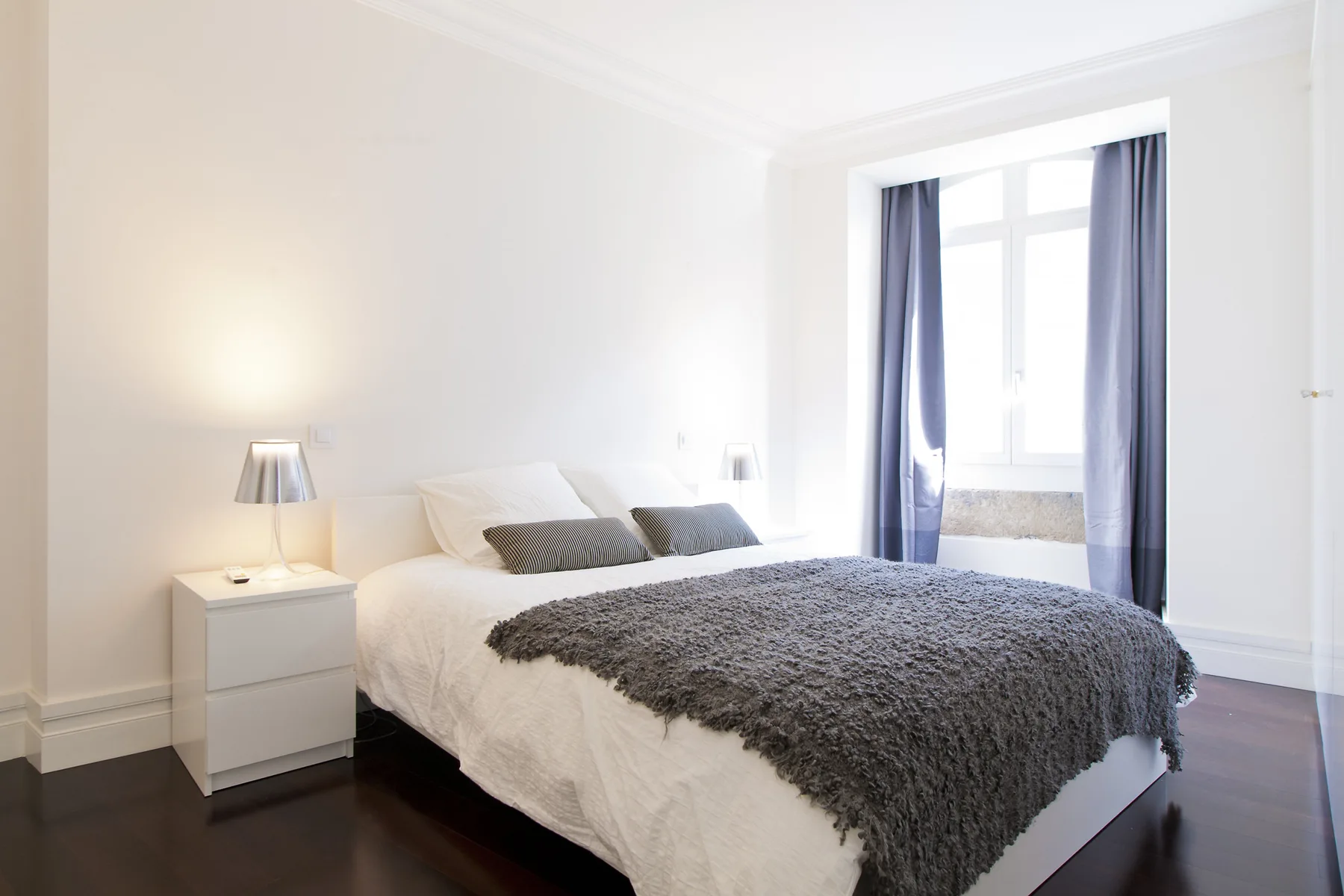 A bright bedroom with a bed and a large window framed by curtains.