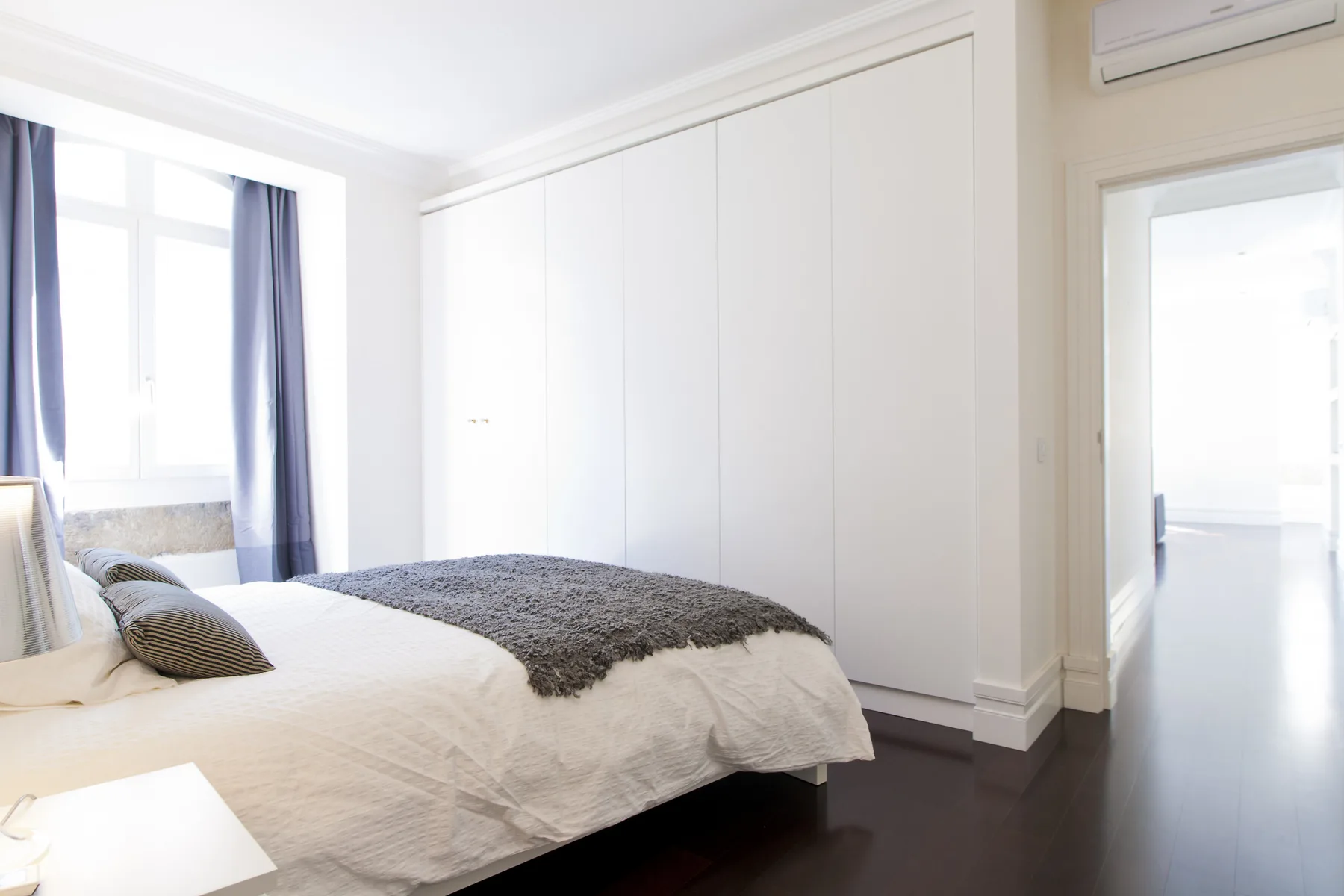 A bright bedroom with a bed beside a large window and an open doorway.