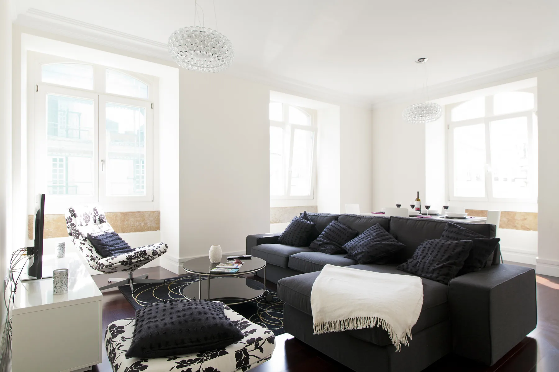 A bright living room with dark seating, large windows, and a glass coffee table.