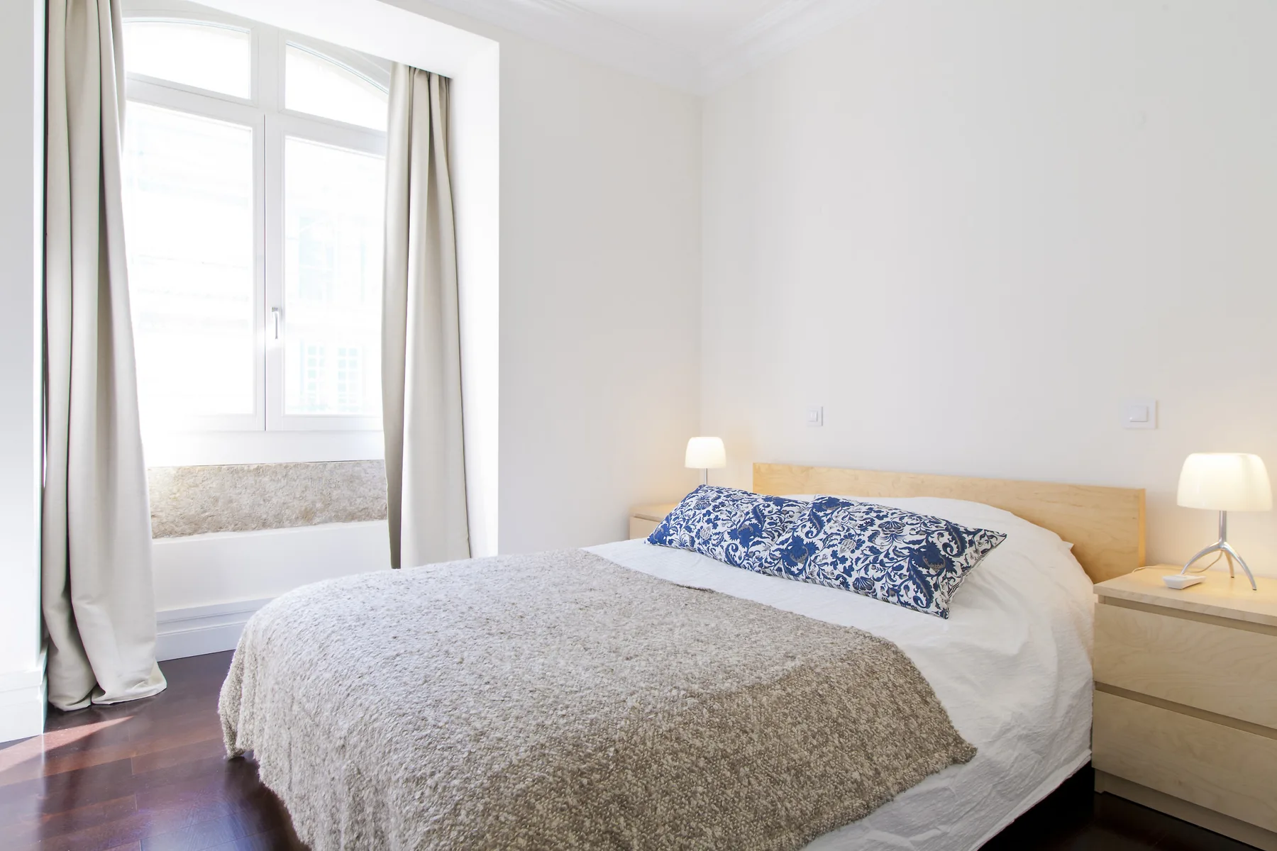 A bright bedroom with a bed dressed in white and patterned blue bedding.