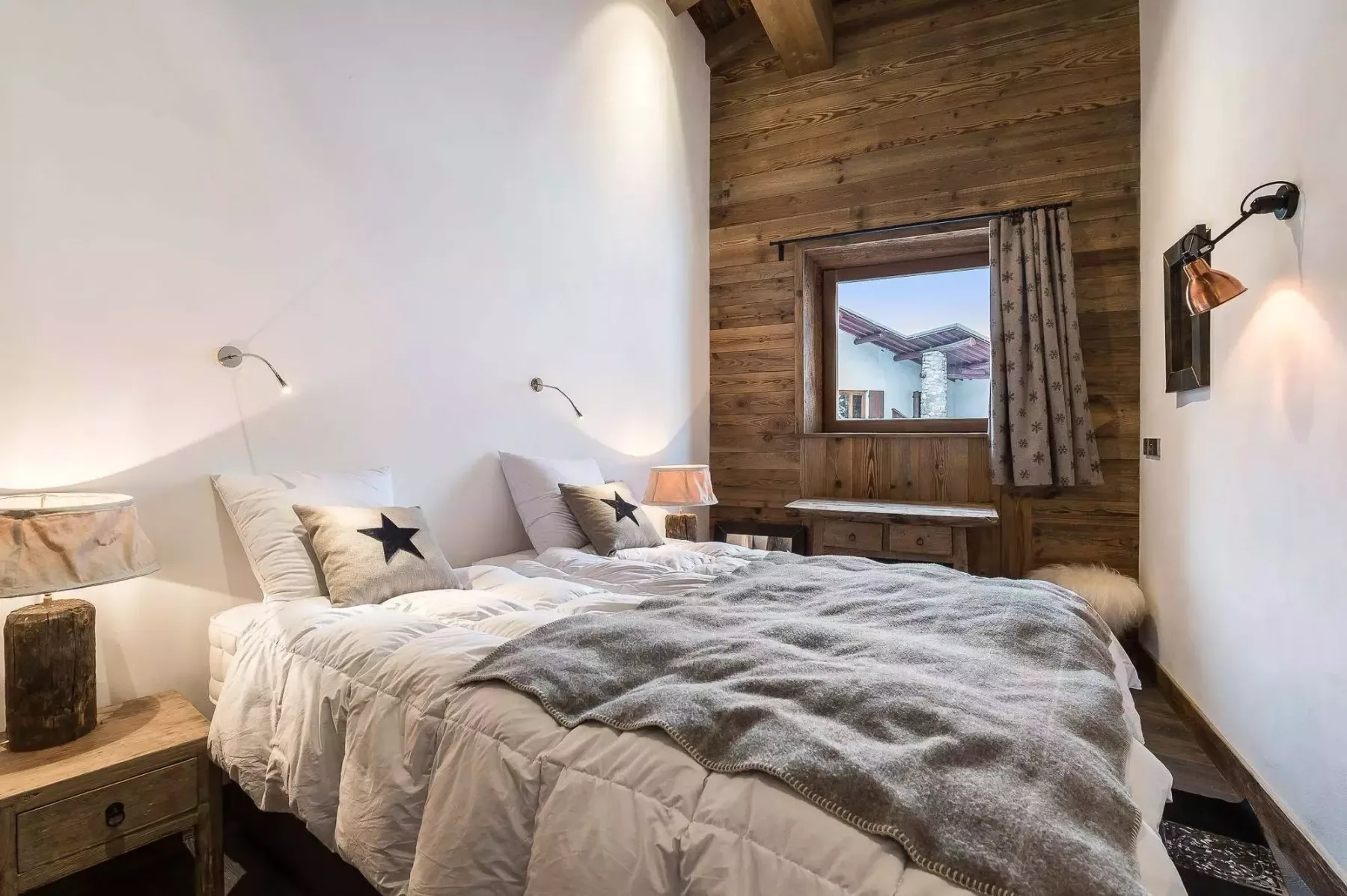 A bedroom with two beds and a window set in a wood-paneled wall.