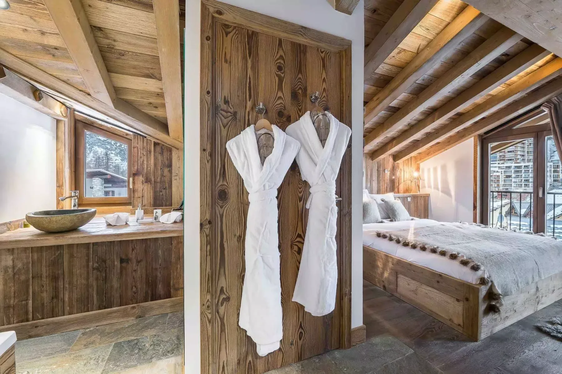 Dormitorio con una cama de madera y dos batas blancas colgadas en una puerta.
