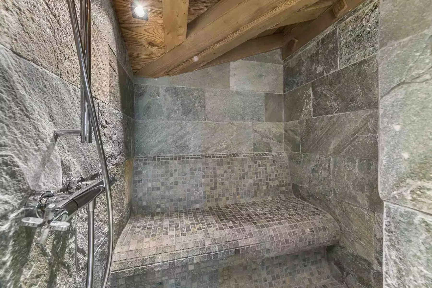 Una zona de ducha revestida de azulejos, con un banco curvo y vigas de madera a la vista.