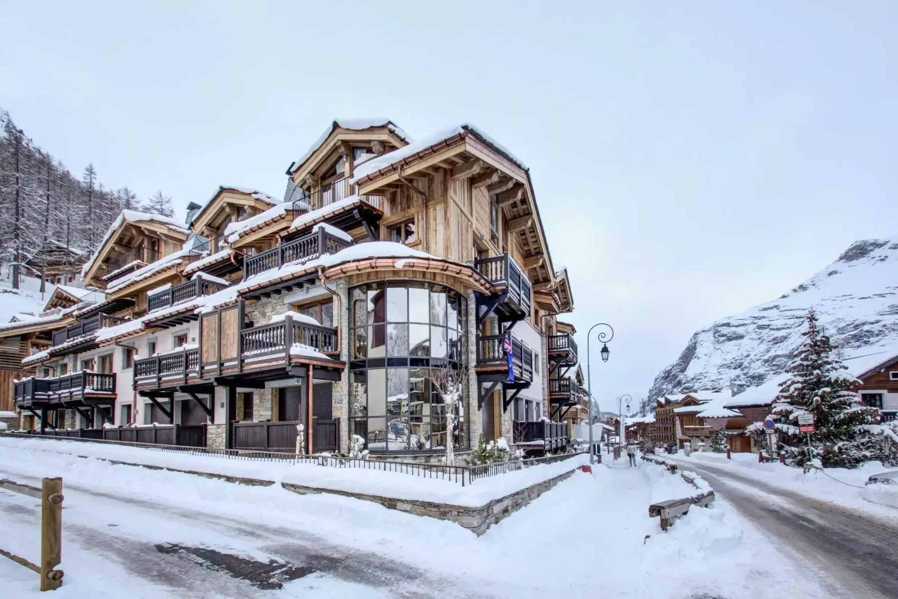 Edificios de montaña cubiertos de nieve bordean una calle bajo un cielo invernal.