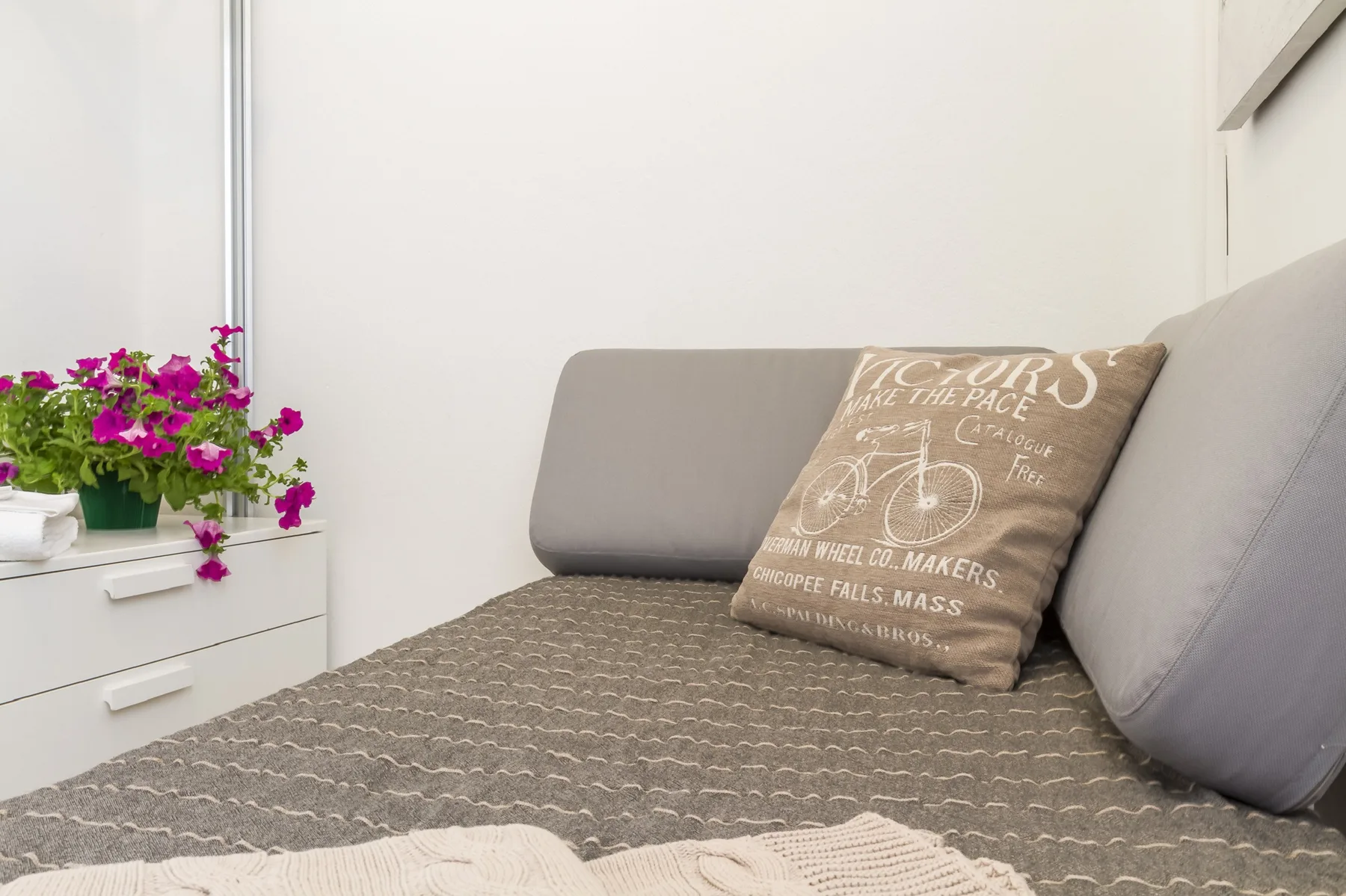 Un dormitorio con una cama bien tendida y una planta con flores al lado.
