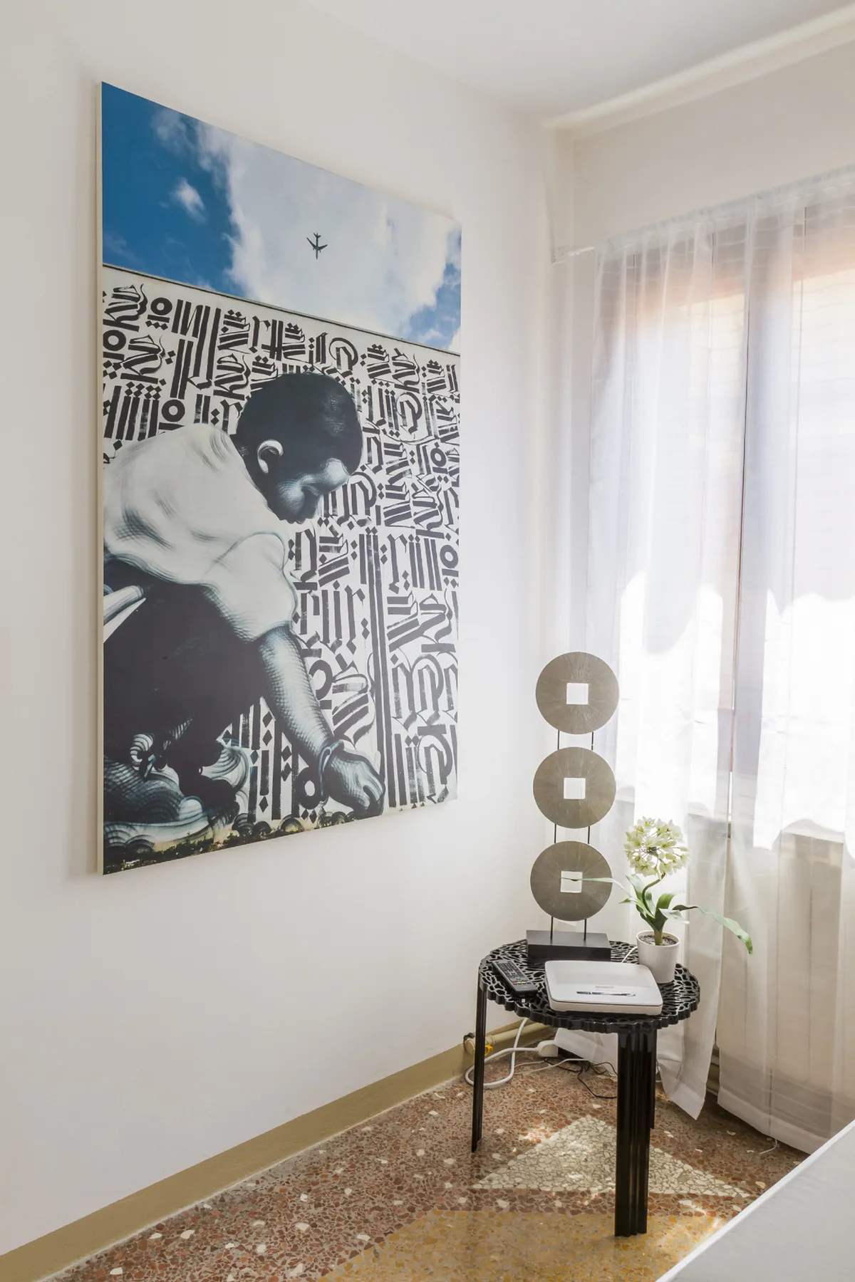 A bright room corner with a small round table beside a sheer-curtained window.