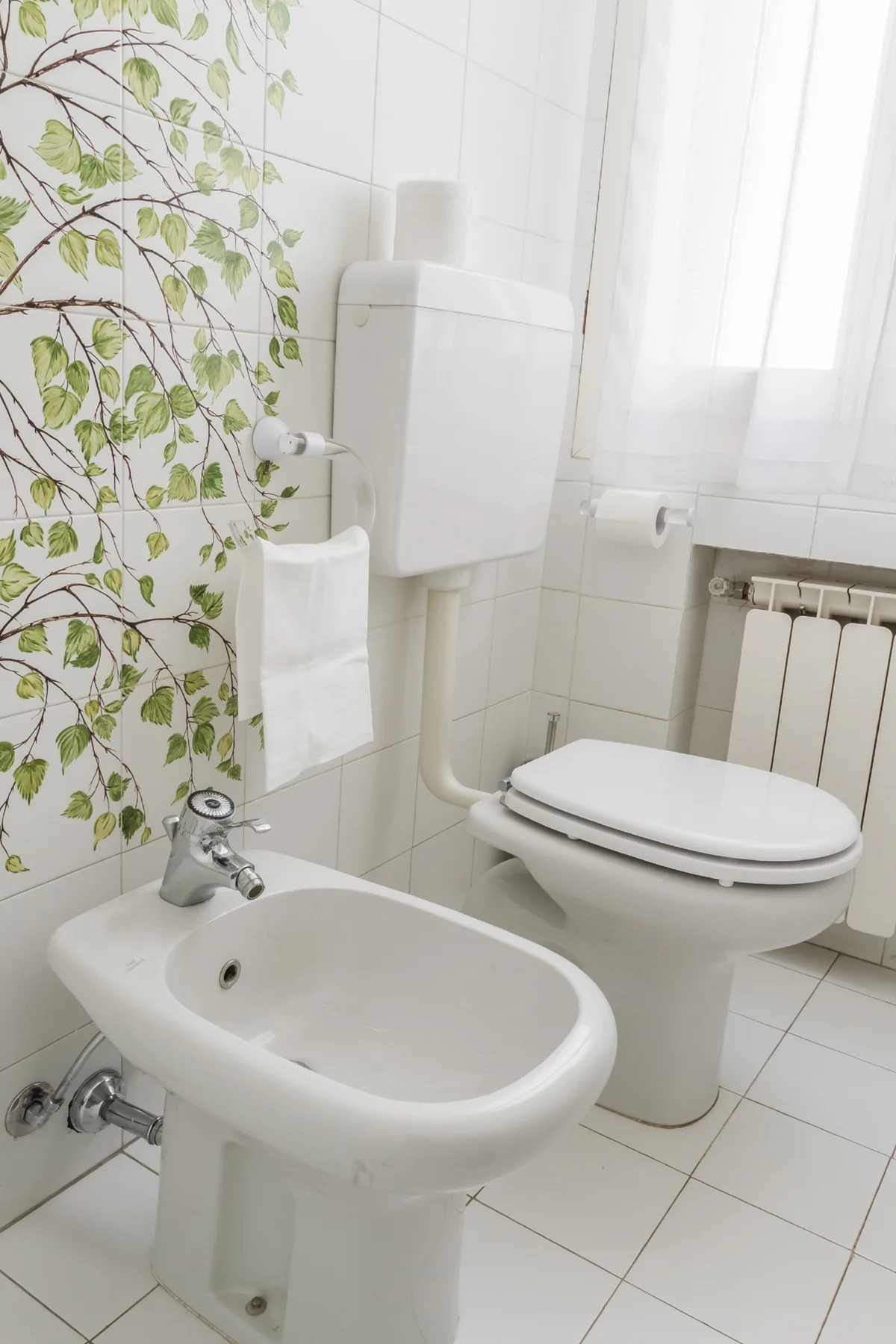 Un baño alicatado con un inodoro y un bidé junto a una ventana.