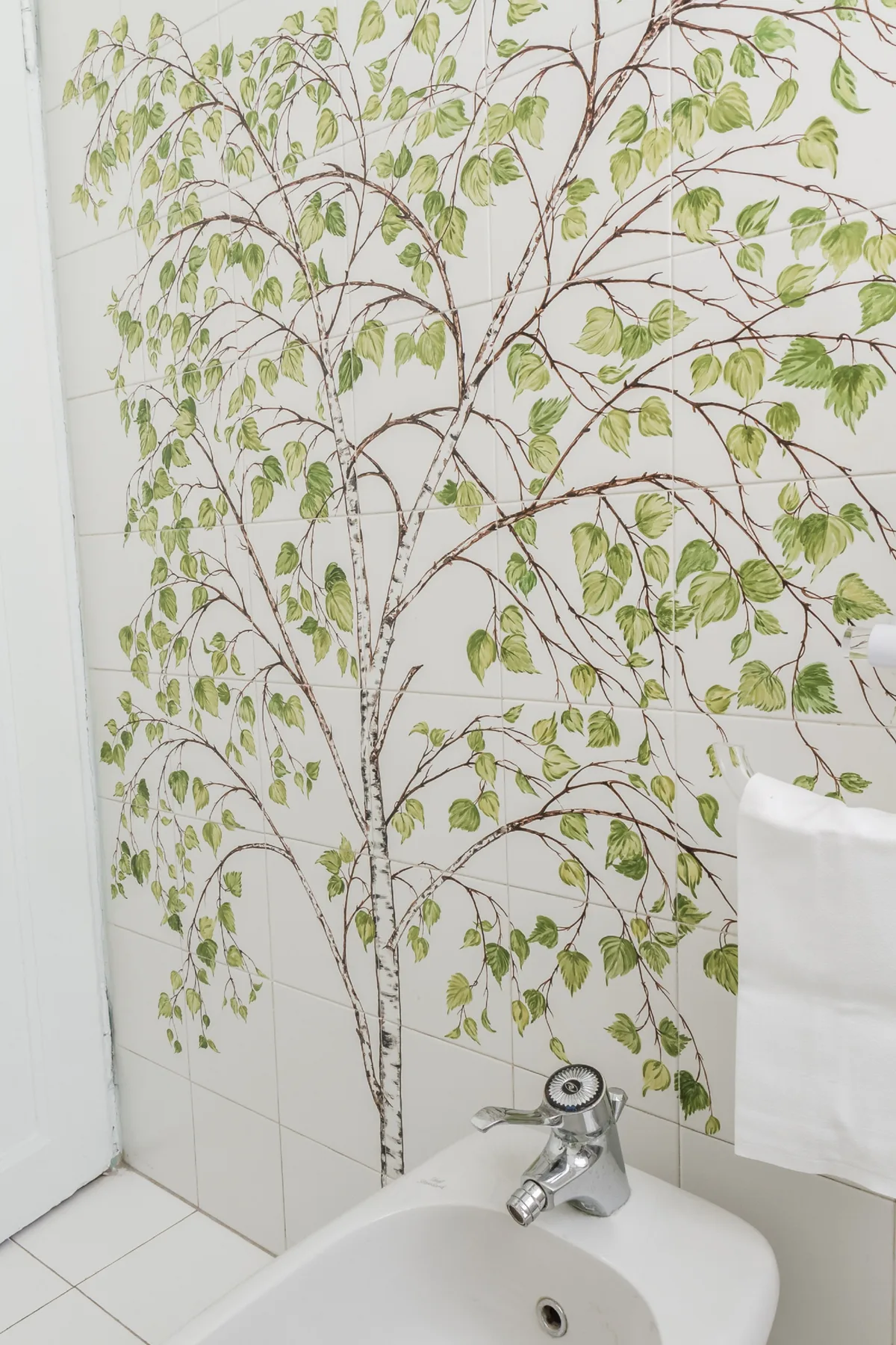 Un lavabo de baño está frente a una pared decorada con un diseño de árbol frondoso.