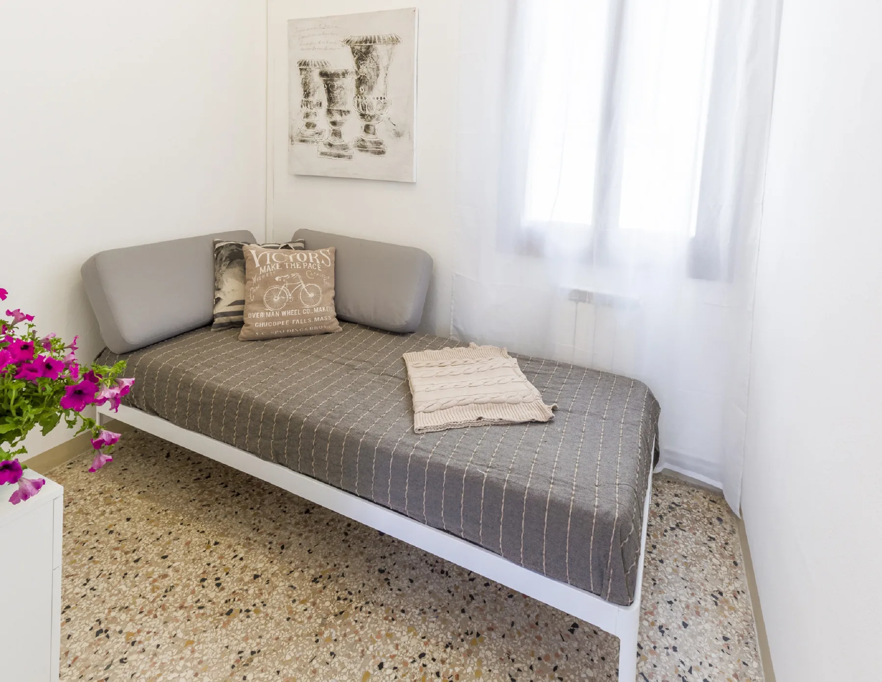 A daybed with gray upholstery sits beside a bright window.