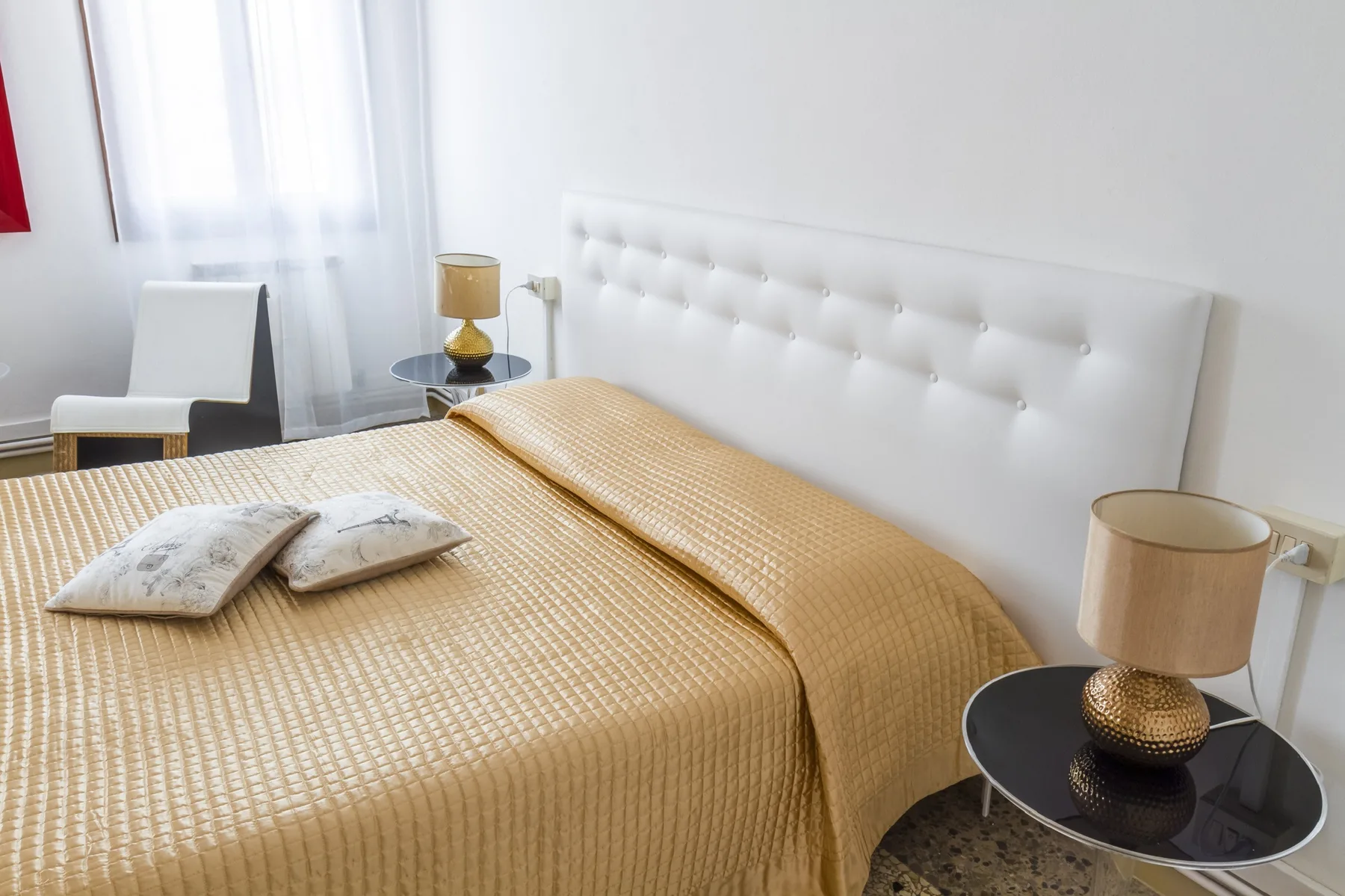 Dormitorio con una cama cubierta con un edredón dorado y un cabecero blanco acolchado.