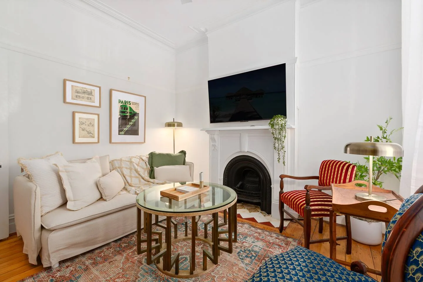 A bright living room with a fireplace, wall-mounted television, and seating around a glass coffee table.