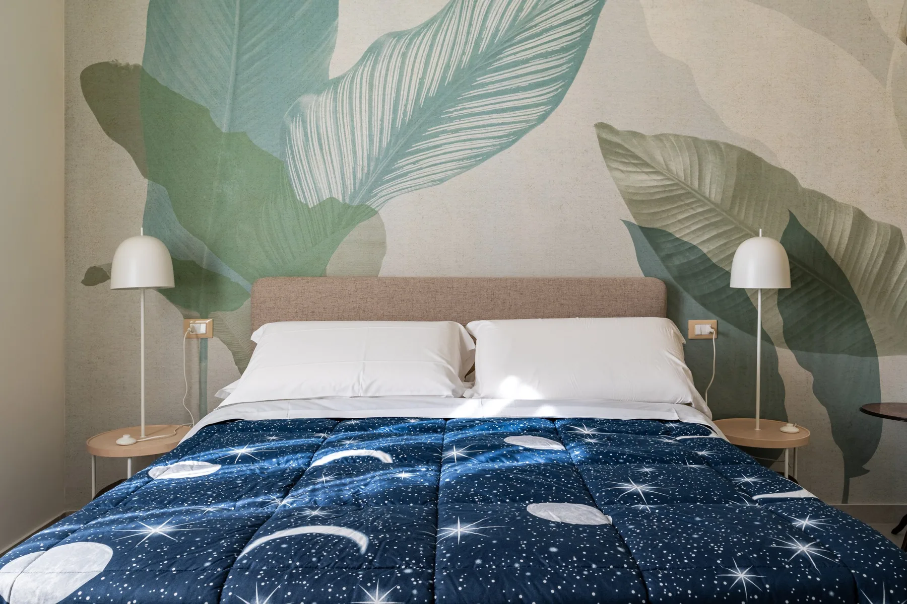 Un dormitorio con una cama cubierta de azul estrellado y arte mural de hojas.