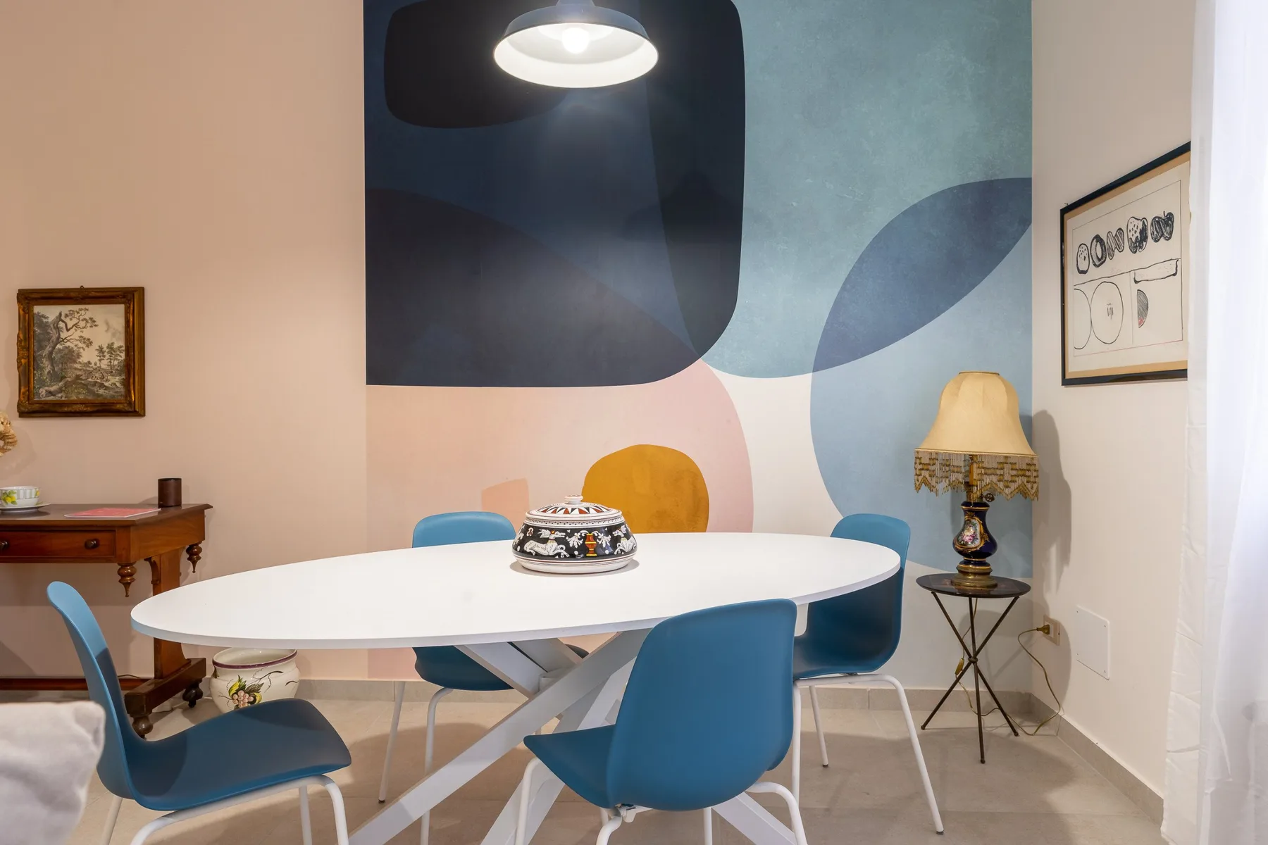 Un comedor con una mesa blanca, sillas azules y arte abstracto colorido en la pared.