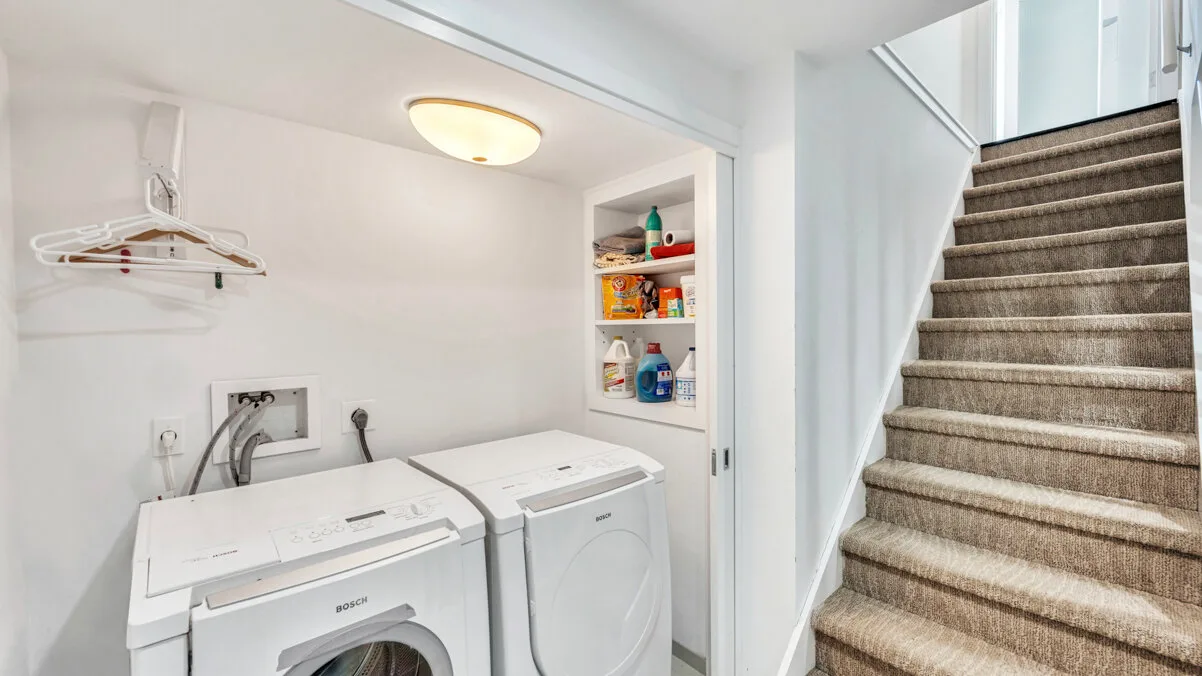 A laundry area with two washing machines beside a carpeted staircase.
