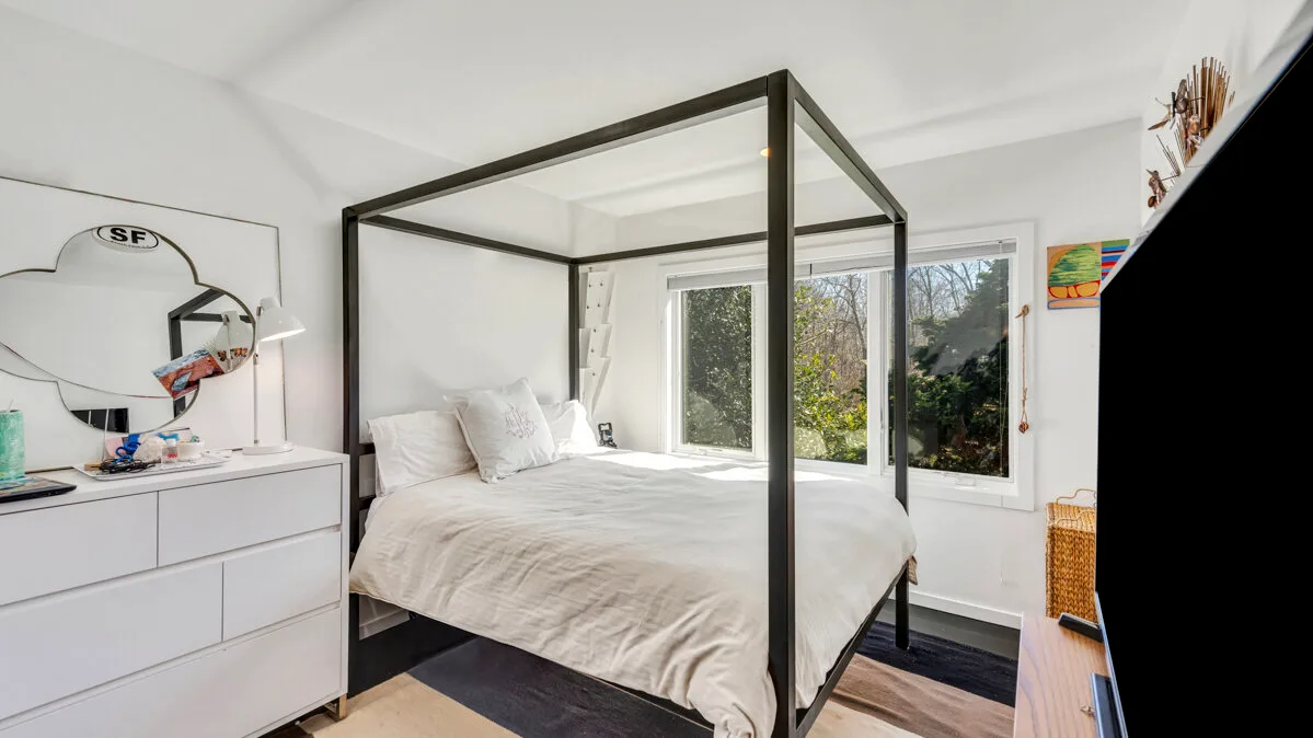 A bright bedroom with a bed beneath large windows.