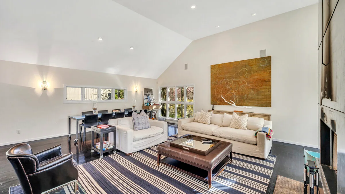 A bright living room has seating arranged around a coffee table on a striped rug.