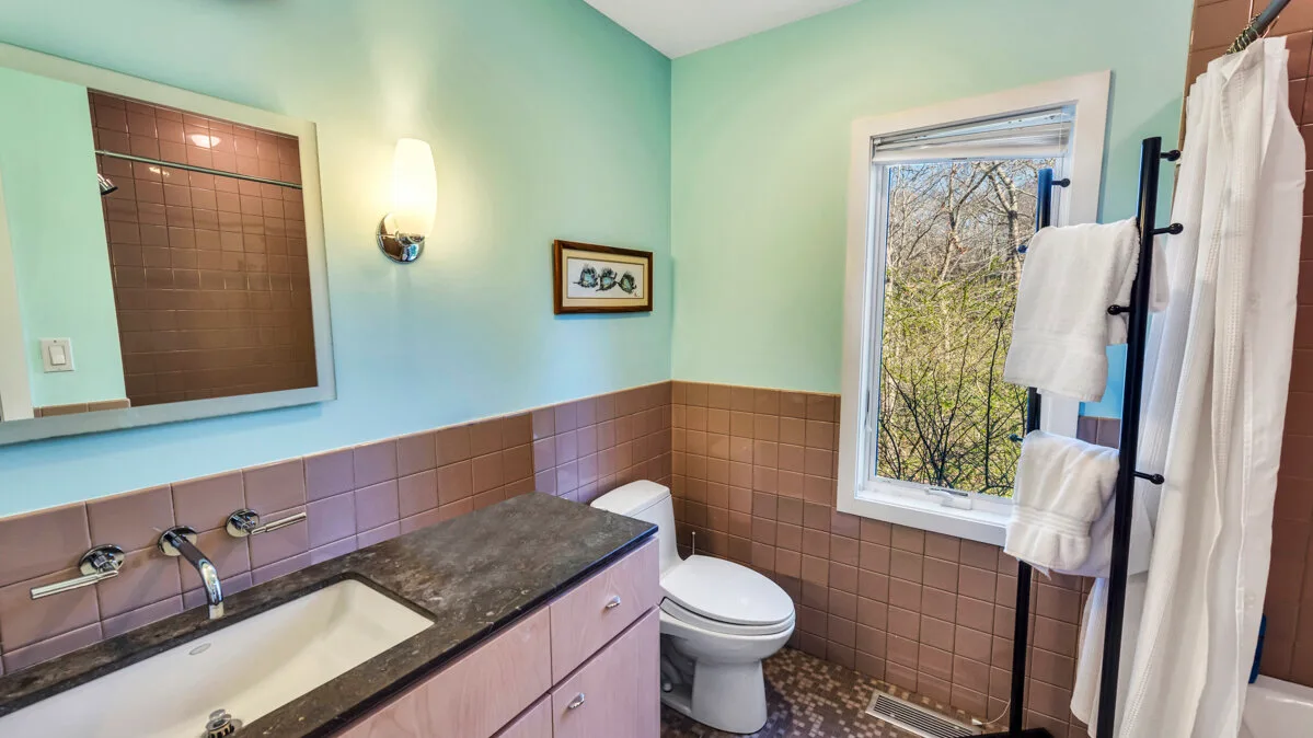 A bathroom with a bathtub, toilet, and window overlooking trees.