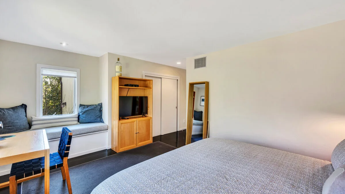 A bedroom with a bed, a television cabinet, and a small seating area by the window.