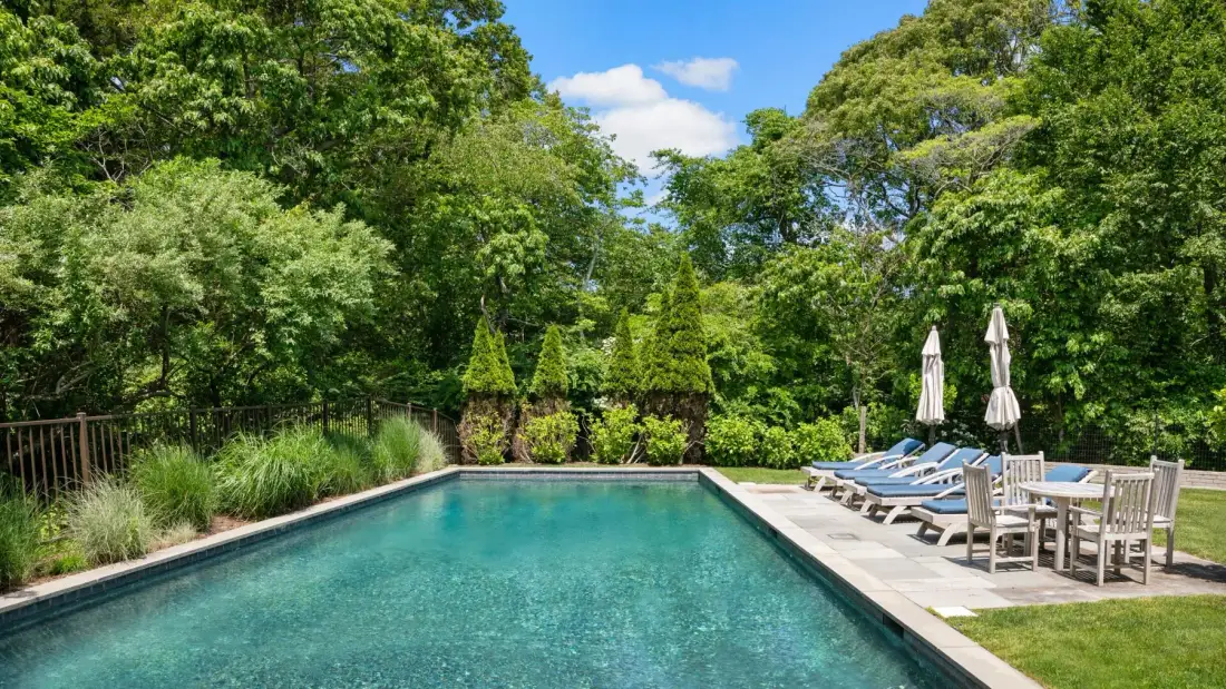 Una piscina al aire libre está rodeada de vegetación y asientos junto a la piscina.