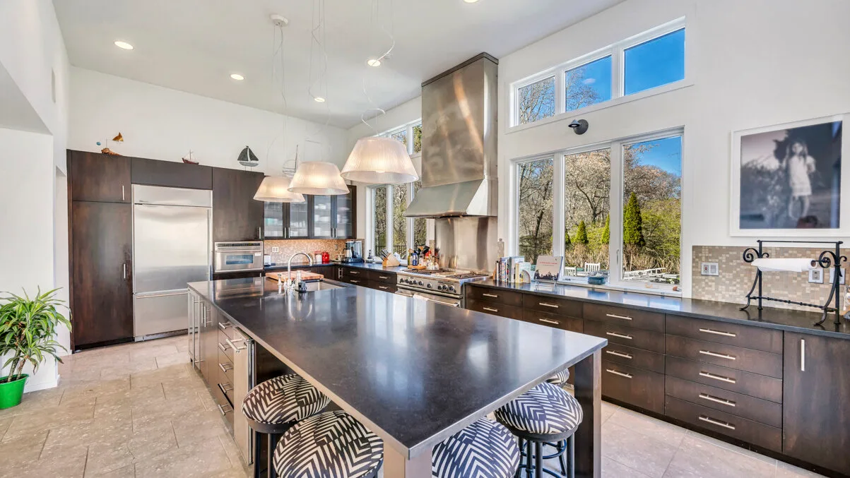 A bright kitchen with a large island, dark cabinets, and wide windows.