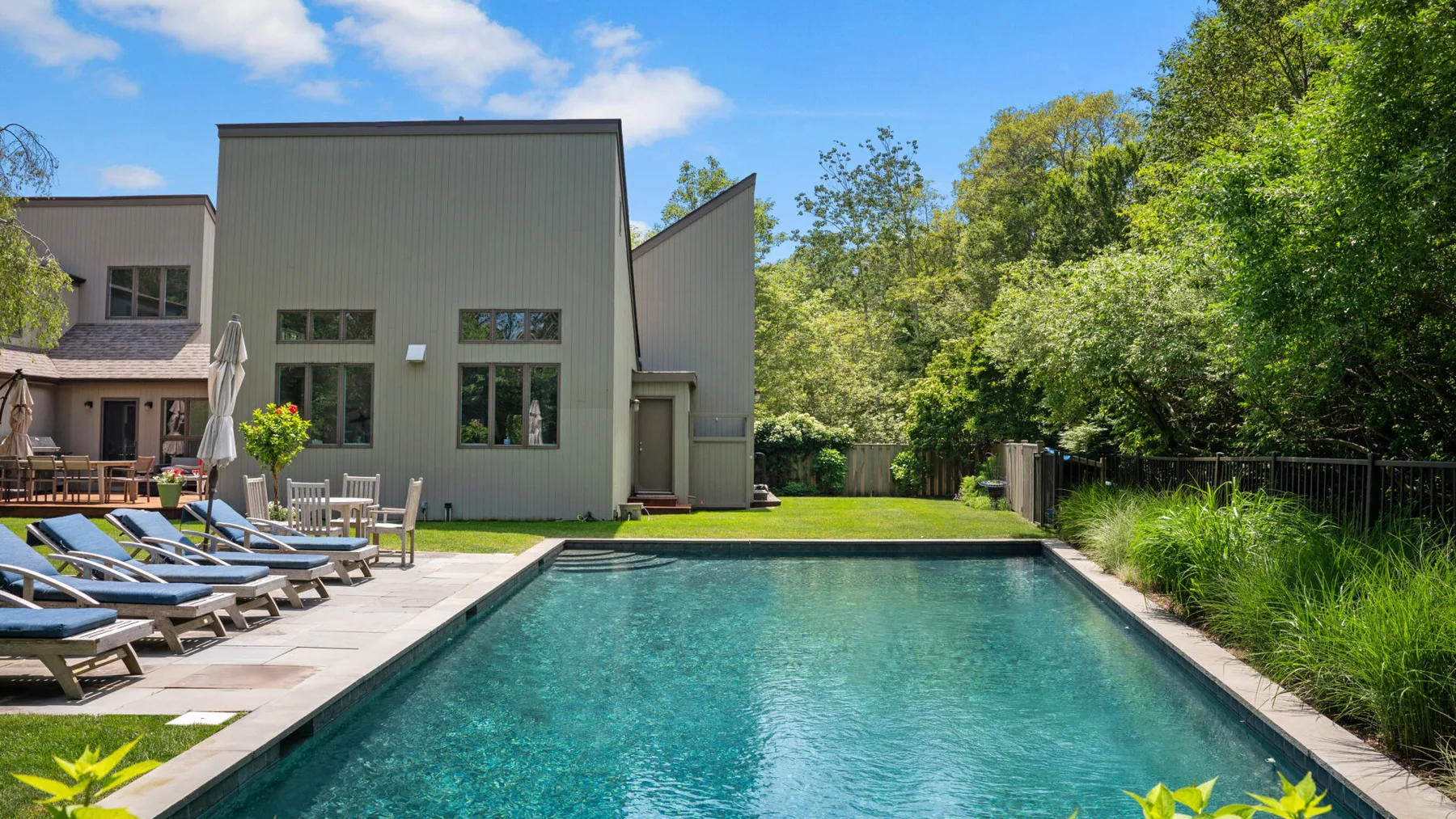 An outdoor swimming pool beside a modern house, with lounge chairs along the deck.