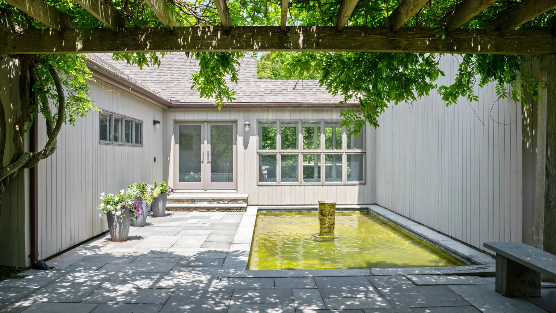 A leafy courtyard with a rectangular water feature beside a light-colored building.