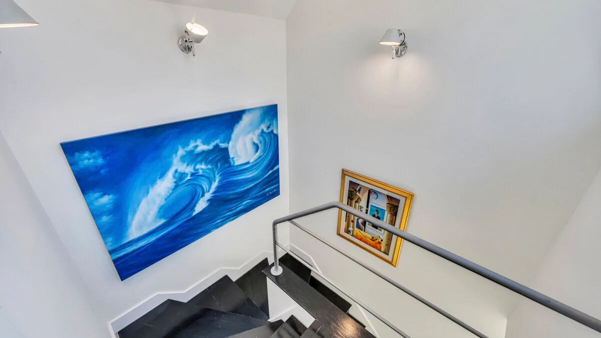 A stairwell with a blue wave painting and framed pictures on the wall.