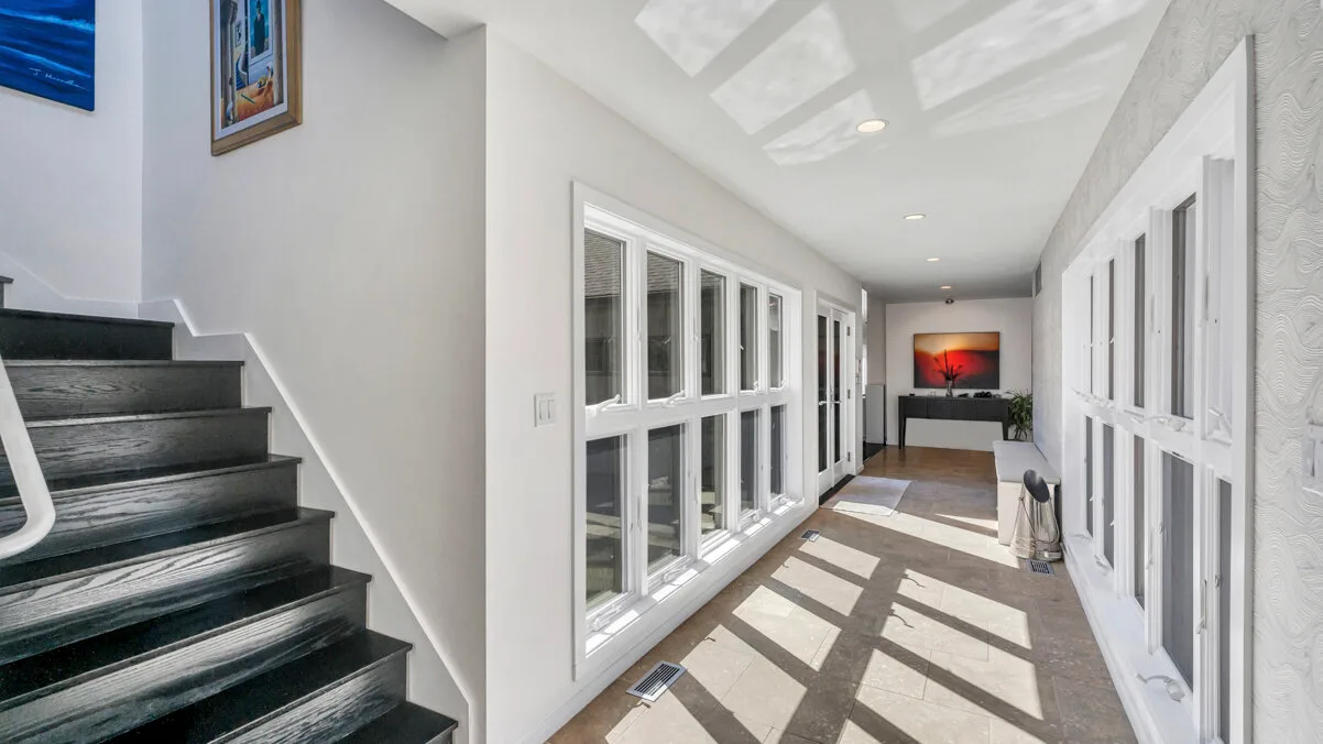 A bright enclosed hallway with large windows and sunlight across the floor.