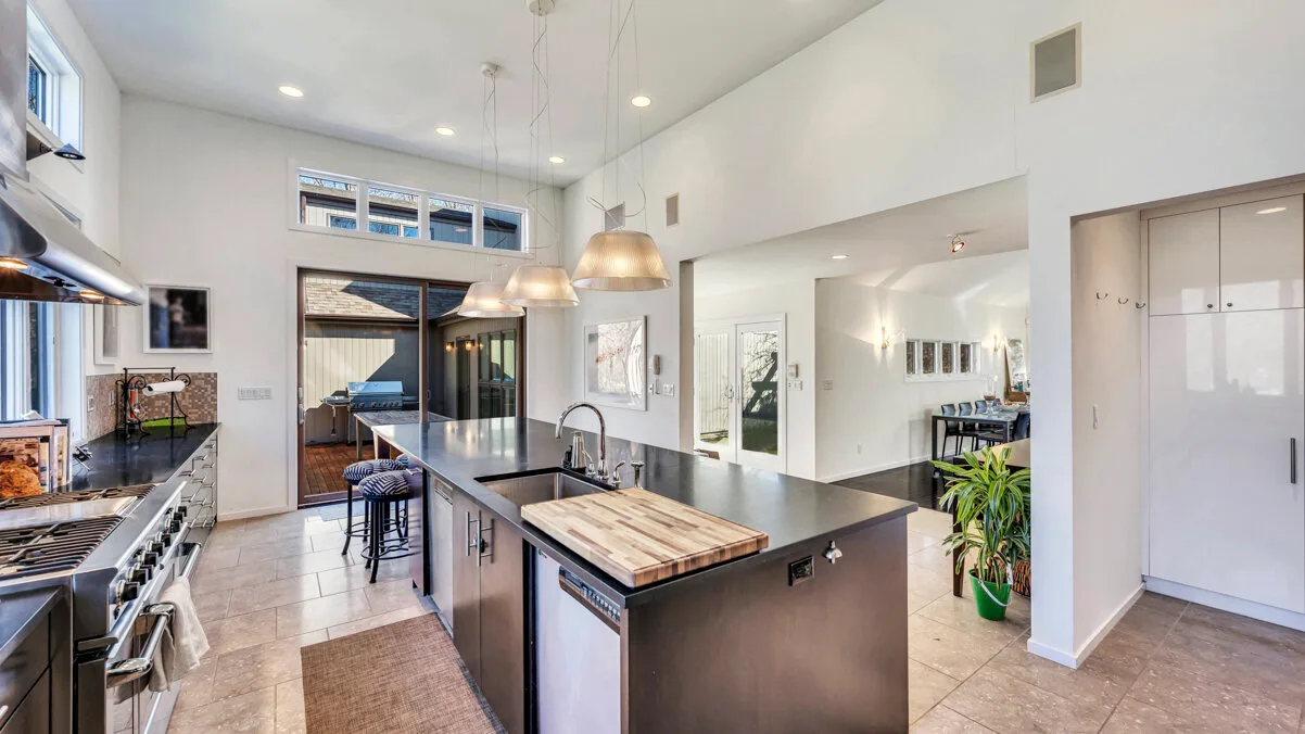A bright kitchen with a large island, pendant lights, and sliding glass doors.