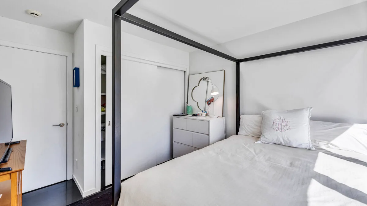 A bright bedroom with a large bed and a dresser beneath a wall mirror.