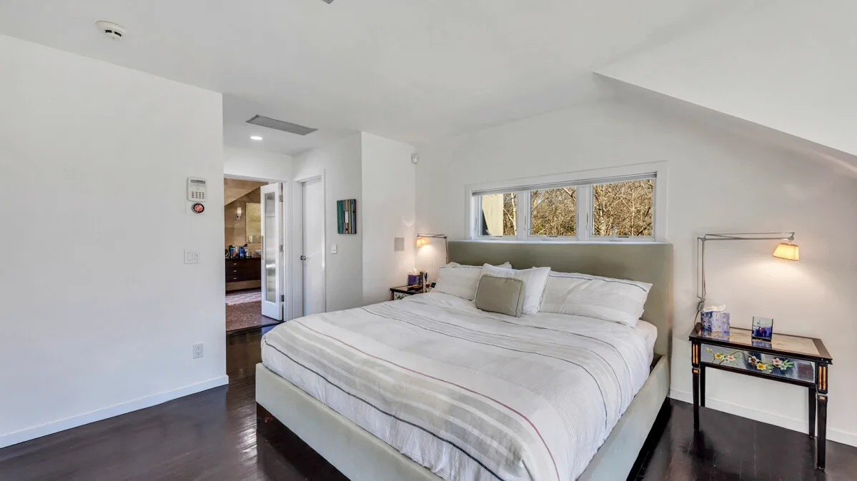 A bright bedroom with a large bed beneath a sloped ceiling.