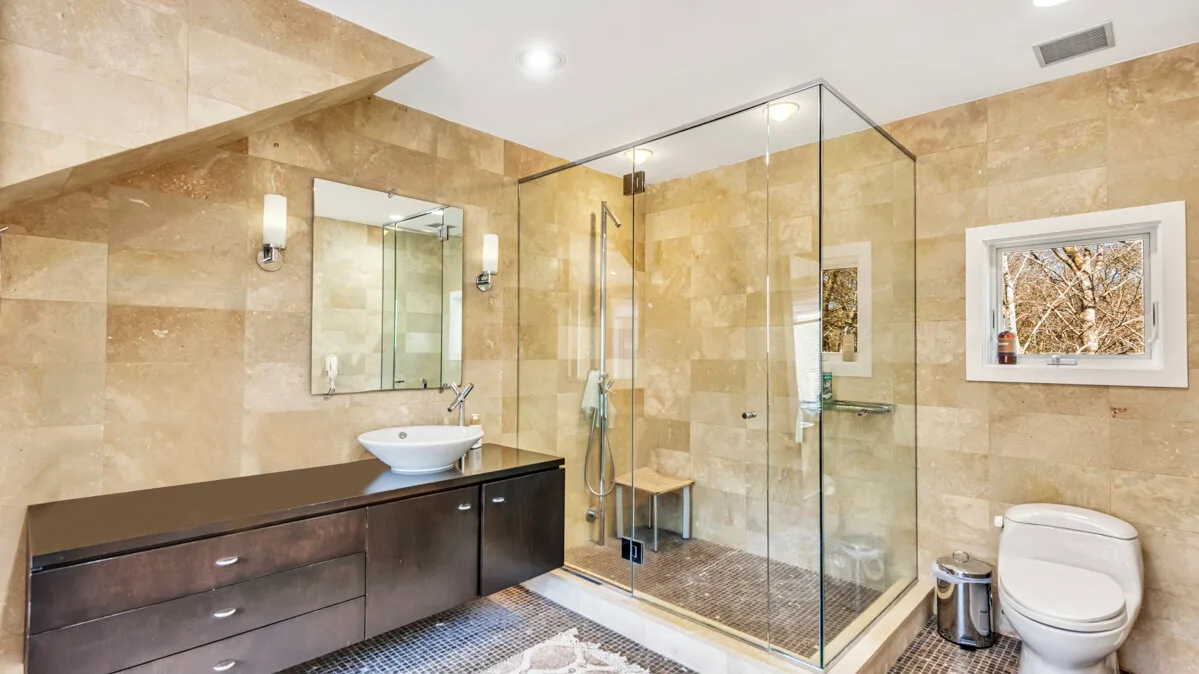 A tiled bathroom with a glass shower, vanity, and toilet.