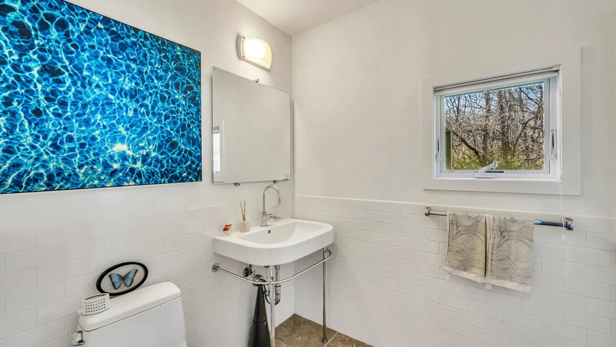 A bathroom with a wall-mounted sink and a window overlooking trees.