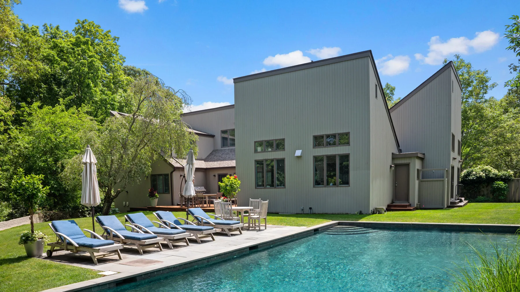 Una casa moderna junto a una piscina, con tumbonas en el patio.