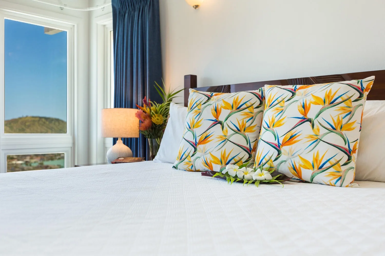 Un dormitorio con una cama bien hecha y almohadas con estampado tropical colorido.