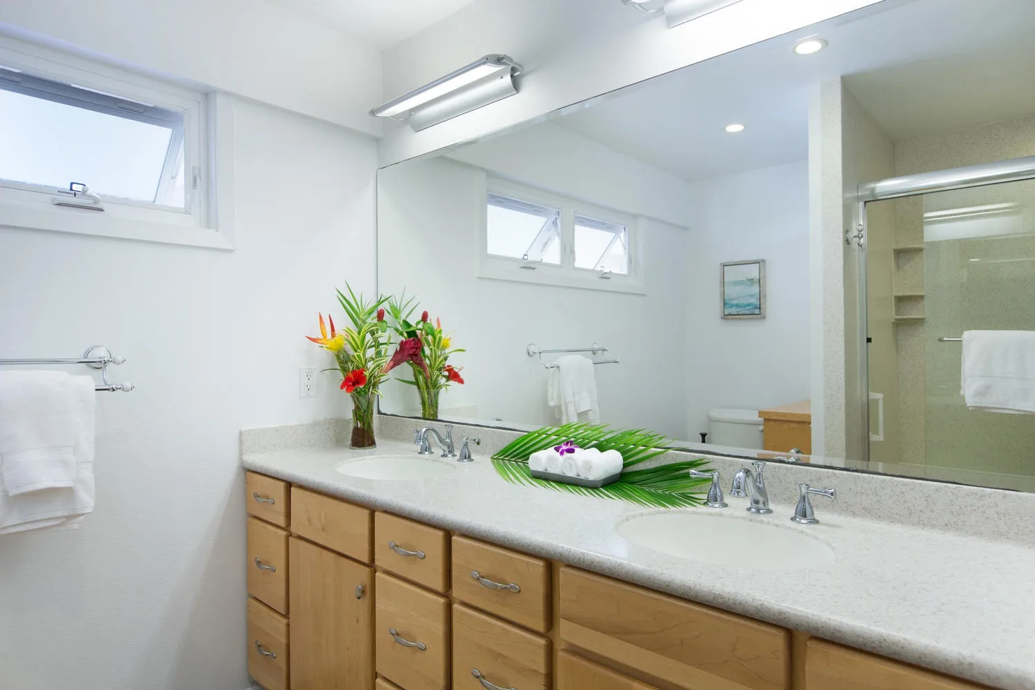 Un lavabo de baño luminoso con un espejo amplio y un arreglo floral.