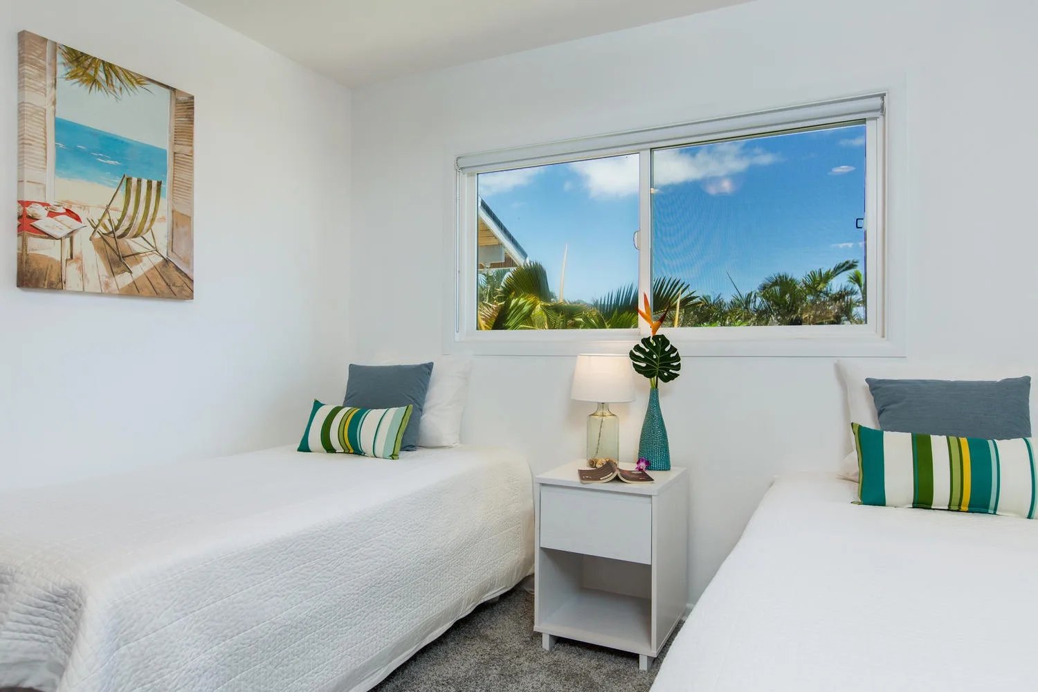 Un dormitorio luminoso con dos camas y una ventana con vistas a palmeras.