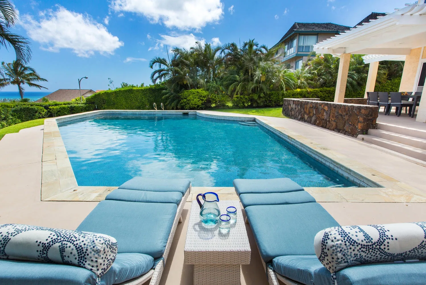 Una piscina al aire libre está rodeada de asientos reclinables y un patio cubierto.