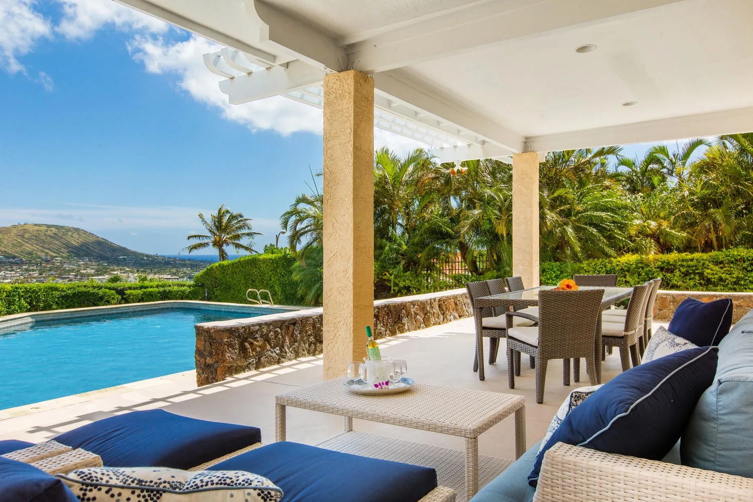 Un patio exterior cubierto con asientos da a una piscina y vegetación tropical.