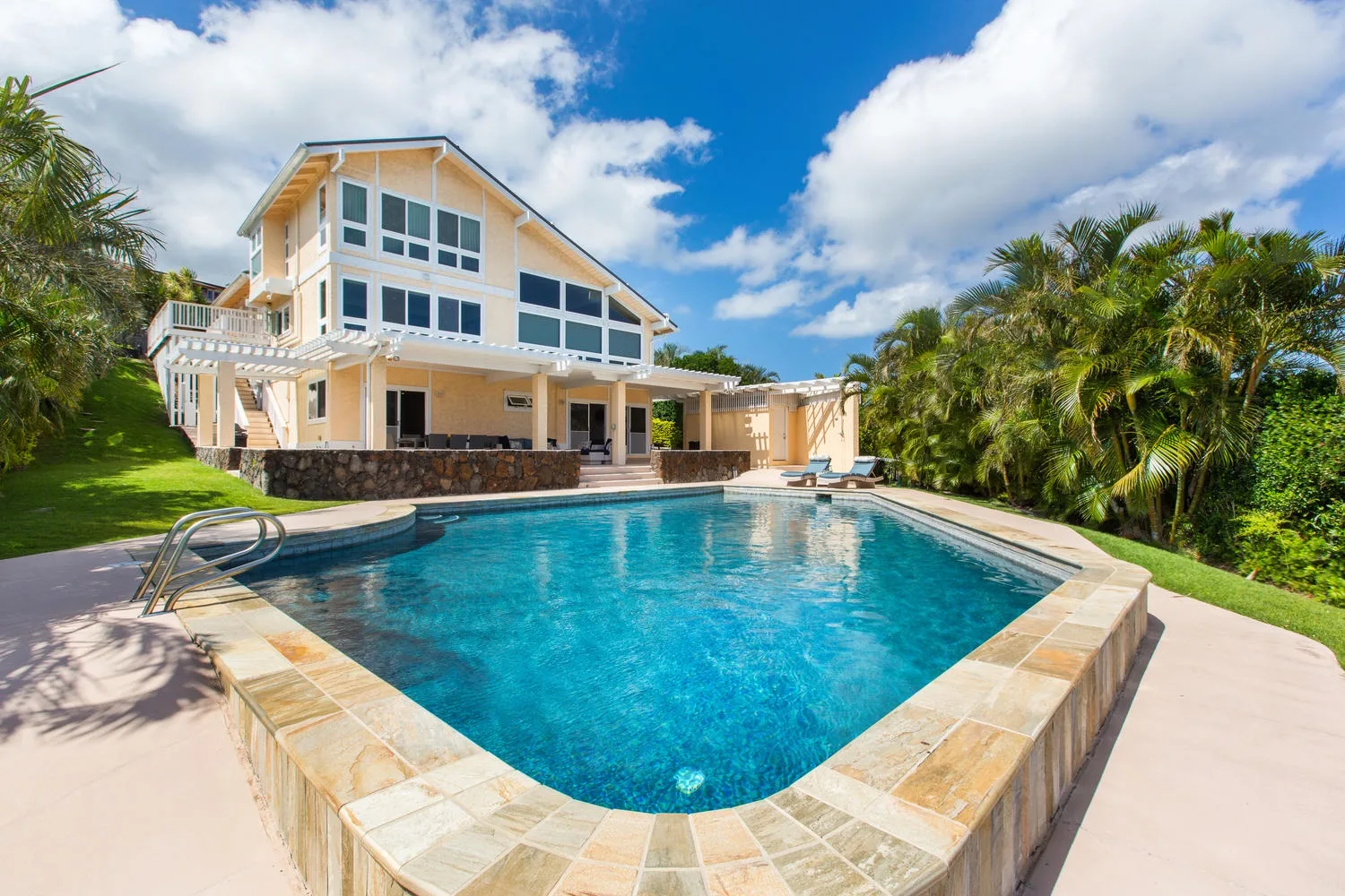 Una piscina está junto a una casa grande, rodeada de palmeras.
