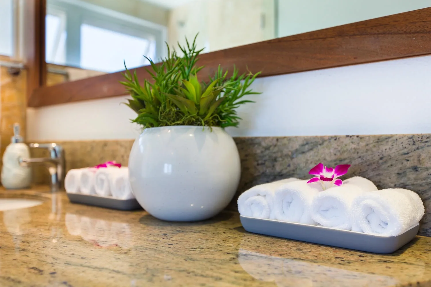 Encimera de baño con toallas blancas enrolladas y una planta en maceta.