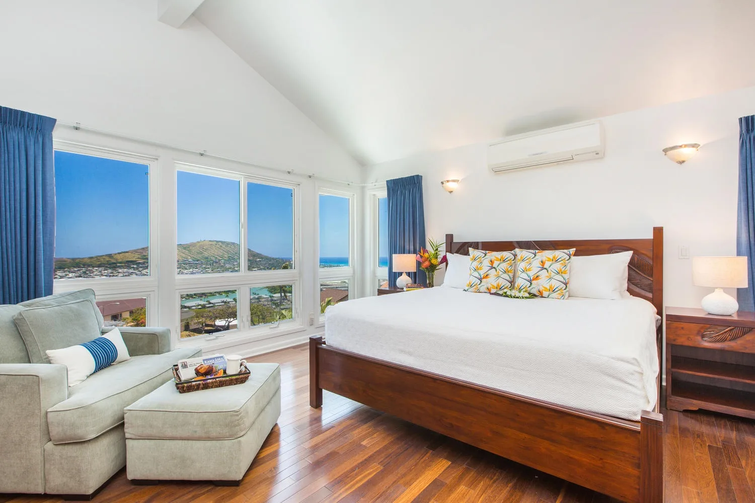 Un dormitorio luminoso con una cama grande, una zona de estar y amplias ventanas con vistas al océano.