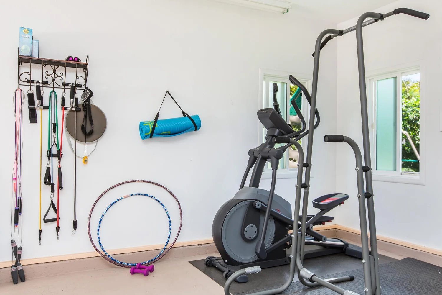 Un gimnasio doméstico con equipo de ejercicio junto a dos ventanas.