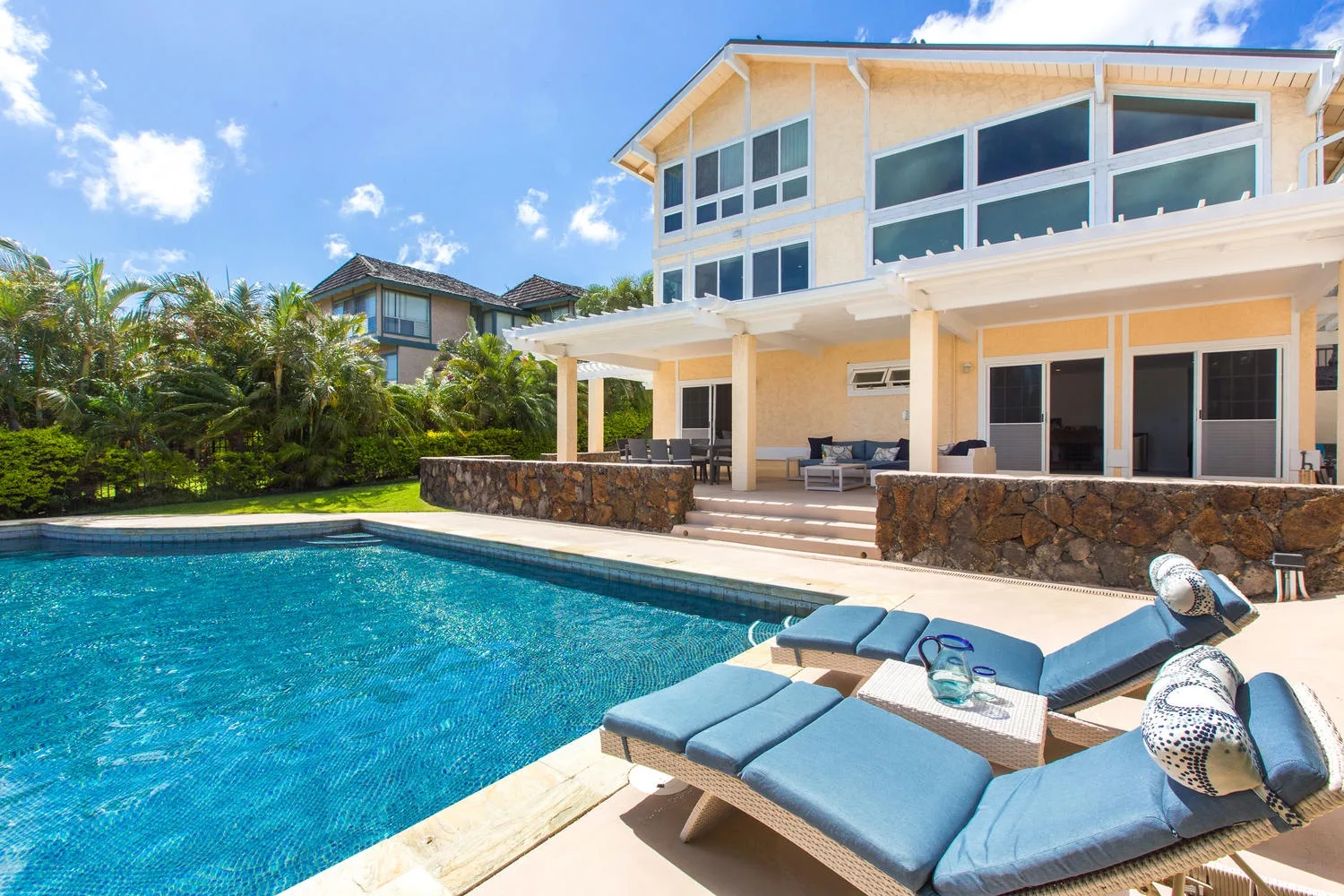 Una piscina junto a una casa moderna, con tumbonas acolchadas en el borde.