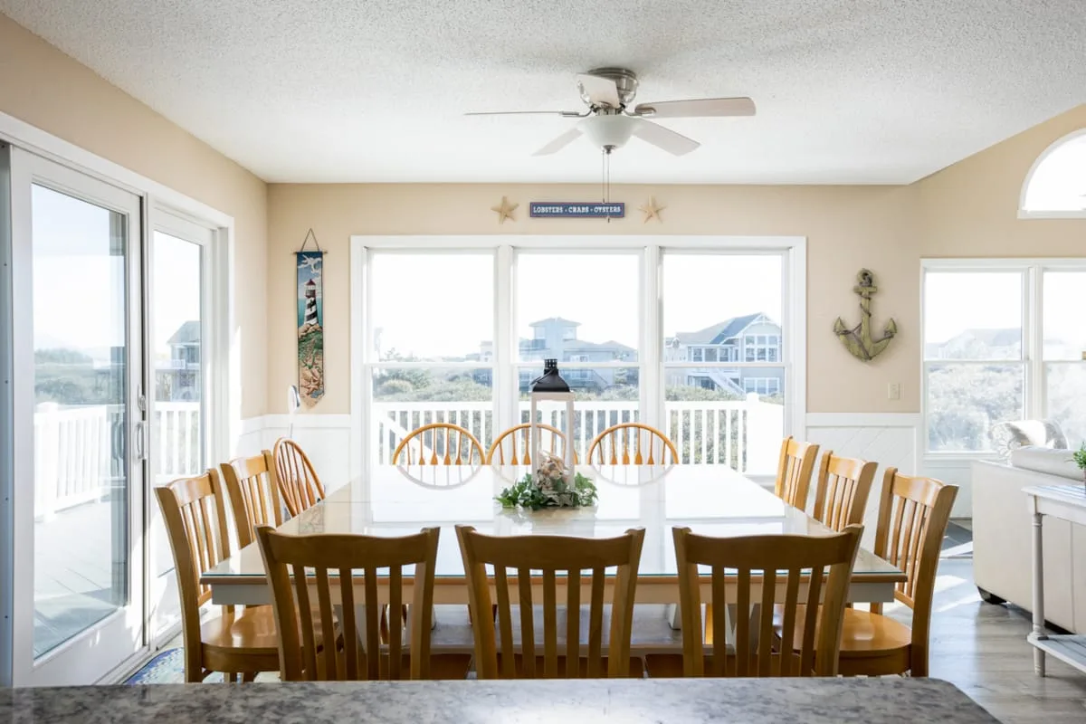 A dining area with a long table and wooden seating beside bright windows.