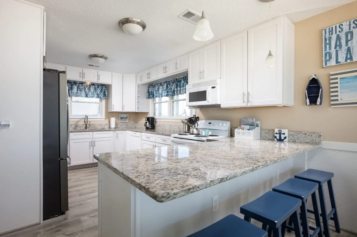 Una cocina luminosa con gabinetes blancos, una isla amplia y taburetes azules.