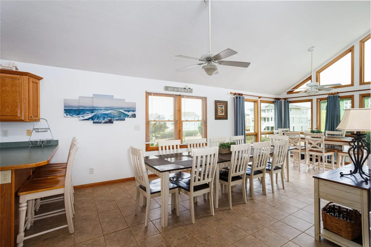Comedor con varias mesas y sillas junto a grandes ventanas.