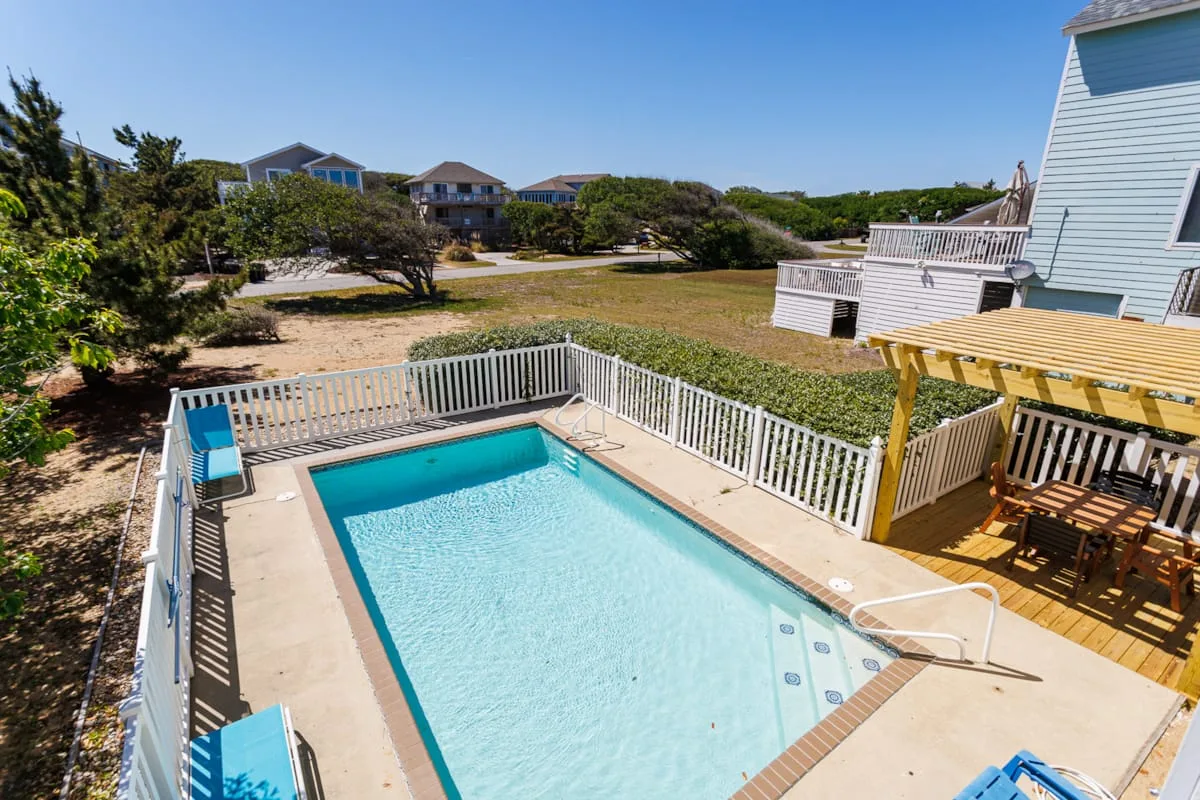 Una piscina está junto a una terraza con barandillas blancas y una zona de estar sombreada.